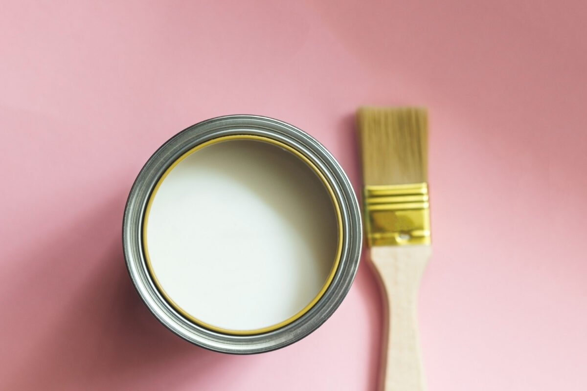 Pinceau avec manche en bois et boîte de peinture blanche ouverte sur fond rose